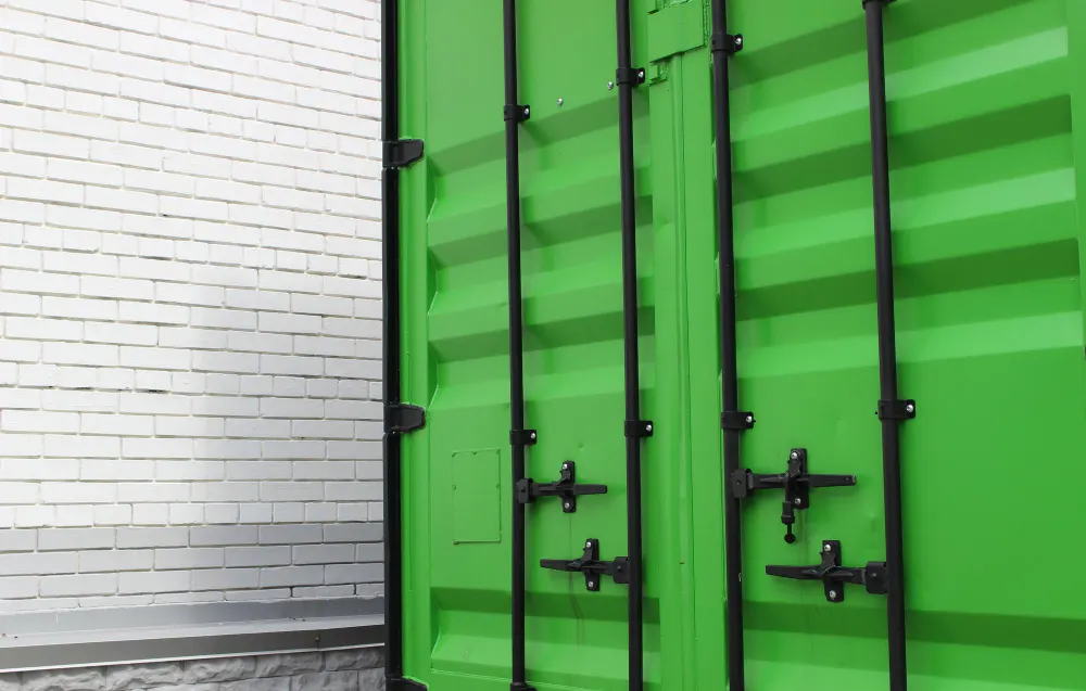 Zbliżenie na jaskrawozielony, stalowy kontener morski. Jego trwała, kofalowa konstrukcja jest idealnym przykładem na nowe i używane kontenery morskie, jakie można znaleźć w naszej ofercie. Widać solidne wrota z czarnymi prętami i mechanizmami ryglowania, typowe dla kontenera magazynowego przeznaczonego do bezpiecznego transportu towarów.